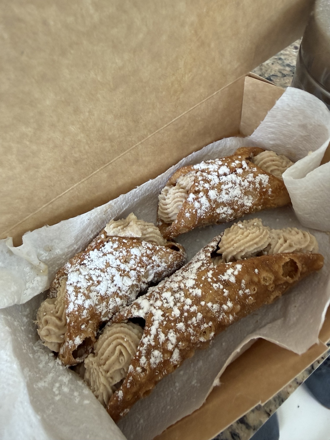 A box of freshly filled cannoli dusted with powdered sugar
